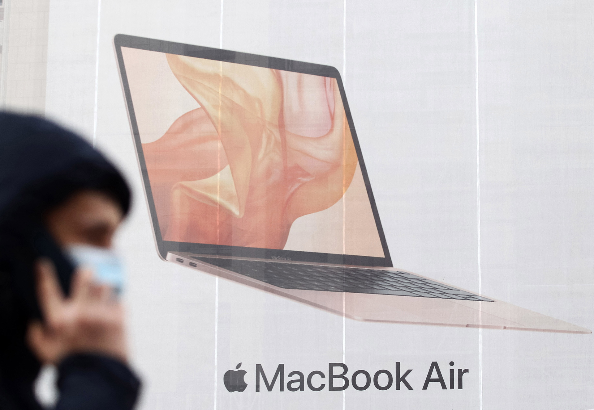 A man wearing a face mask as a preventive measure walks past a Macbook Air by Apple advert