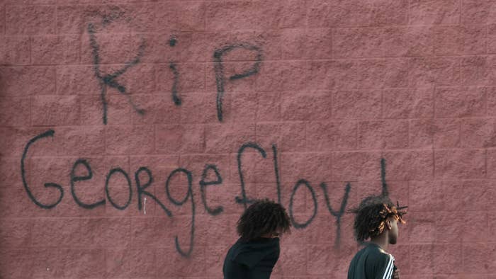 Two men walk past a wall that has &quot;RIP George Floyd&quot; .