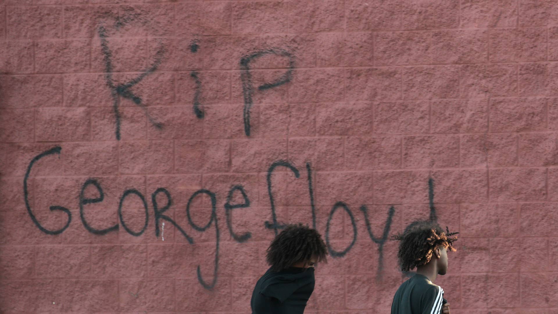 Two men walk past a wall that has "RIP George Floyd" .