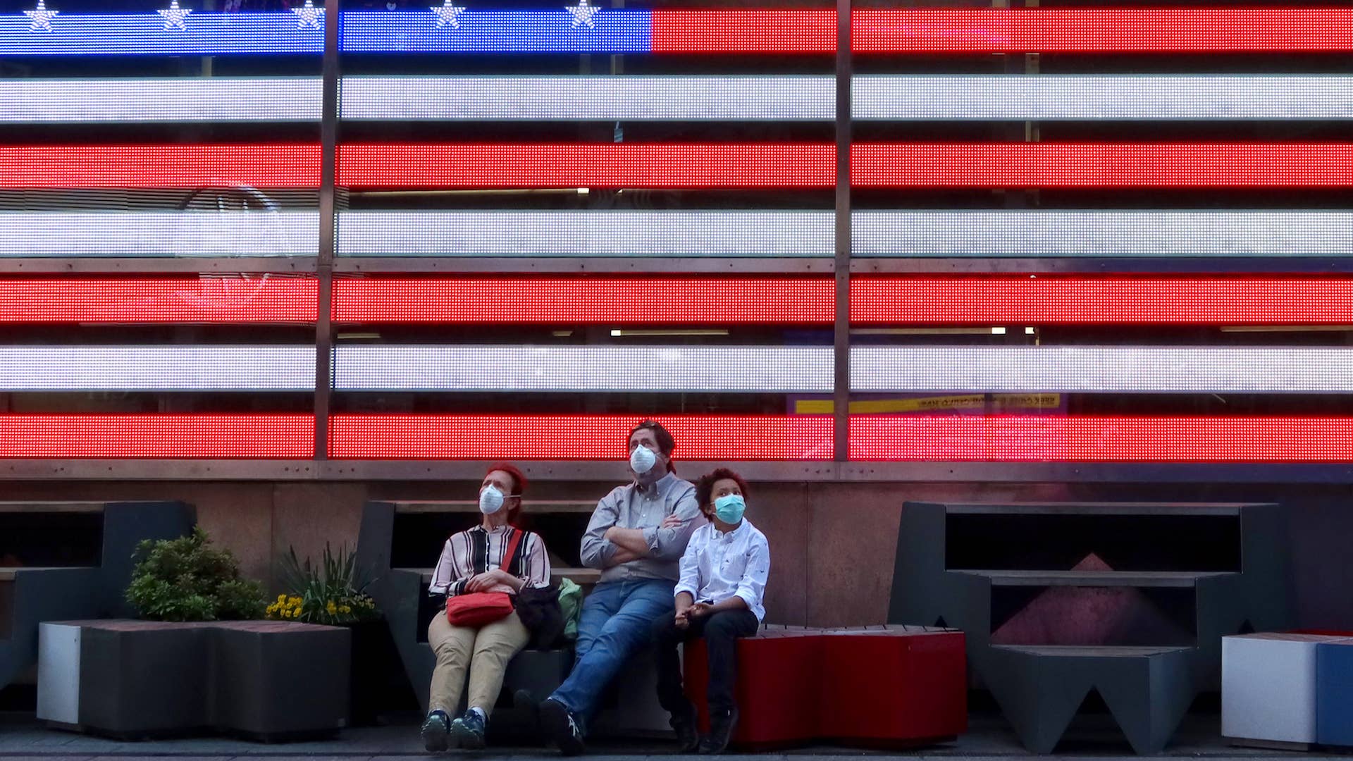 People wear masks as they sit in under an American flag in Times Square .