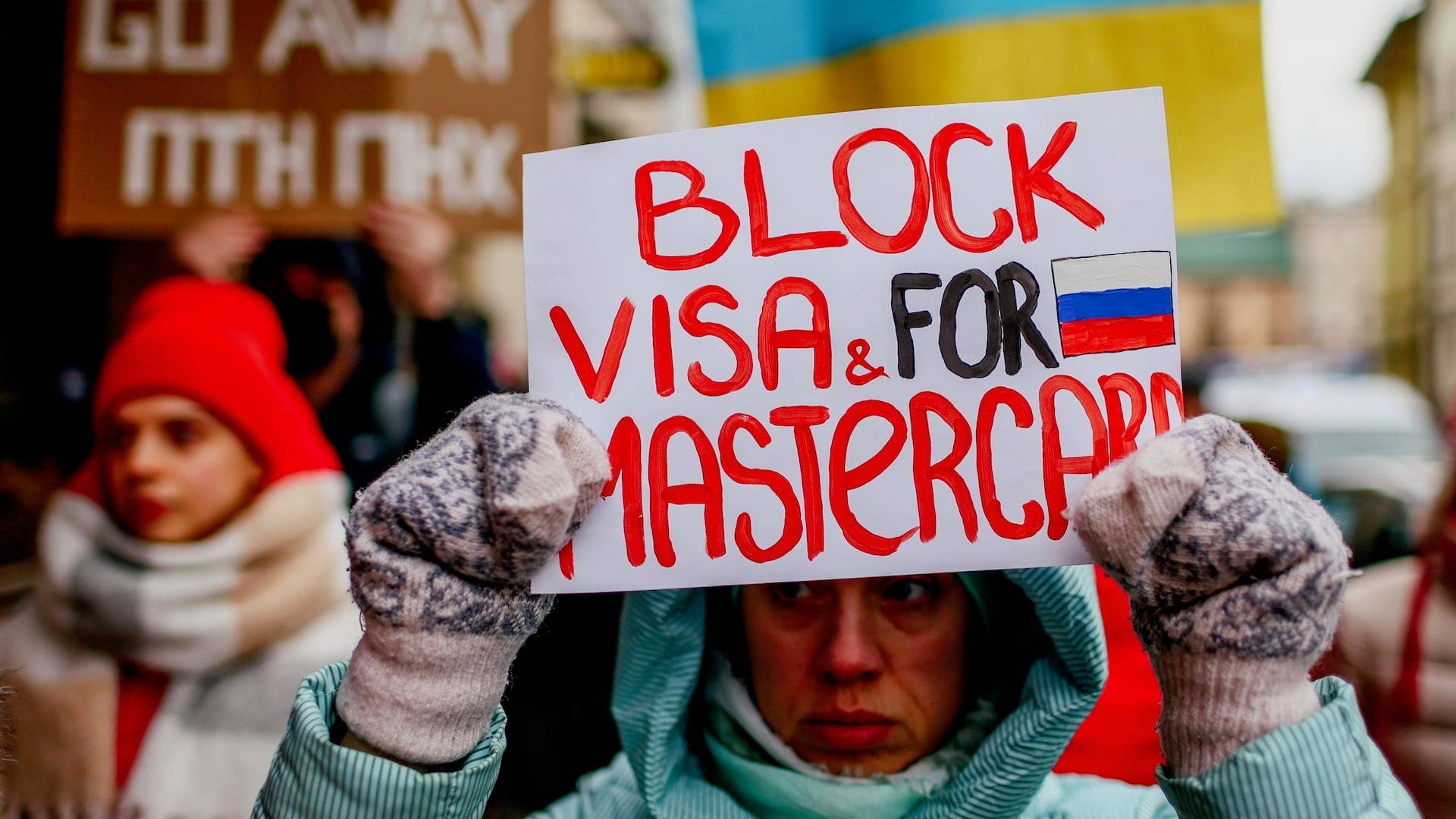 A protester is seen holding a placard that says "Block Visa and Mastercard for Russia"