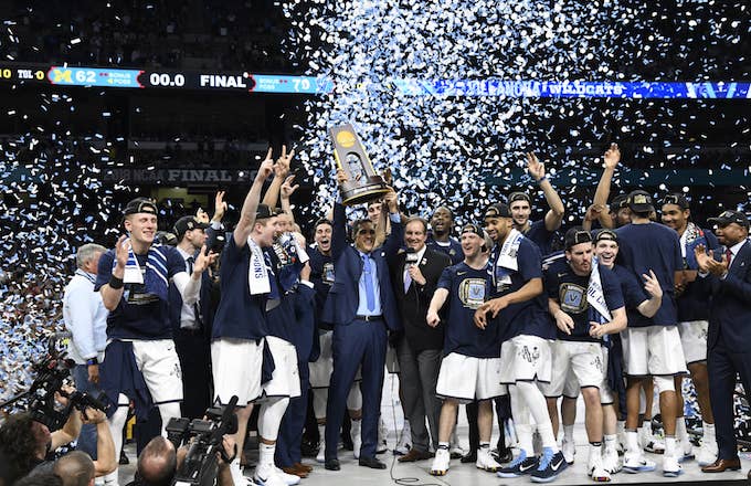 Villanova coach Jay Wright victorious, holding up National Championship trophy with players.