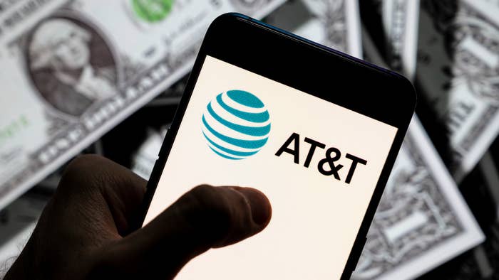 In this photo illustration, an AT&amp;T logo seen displayed on a smartphone with USD (United States dollar) currency in the background.
