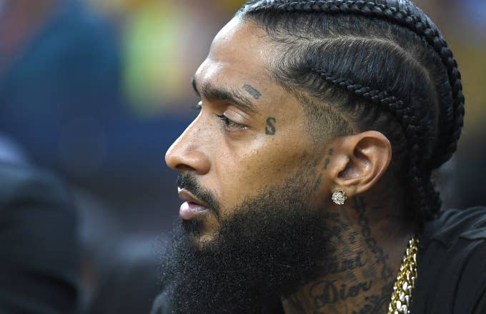 Rapper Nipsey Hussle sitting at courtside looks on during an NBA basketball game
