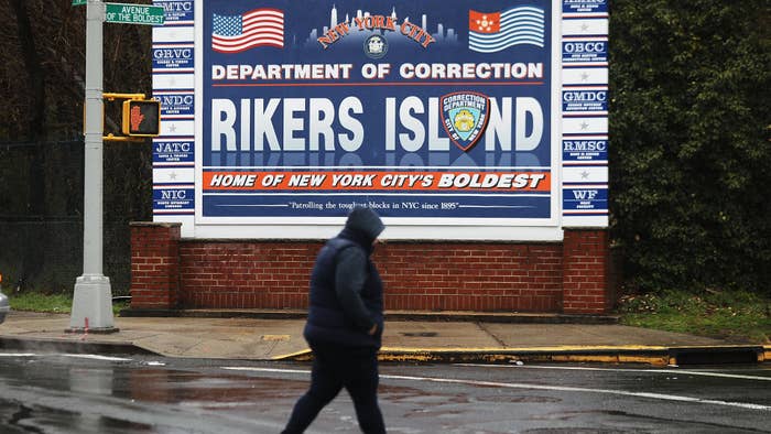 A woman walks by a sign at the entrance to Rikers Island.