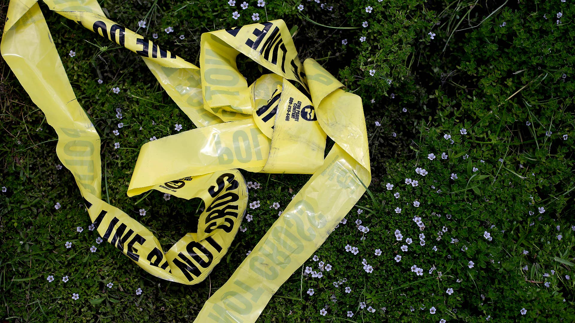 Yellow police crime scene tape rests in the grass.