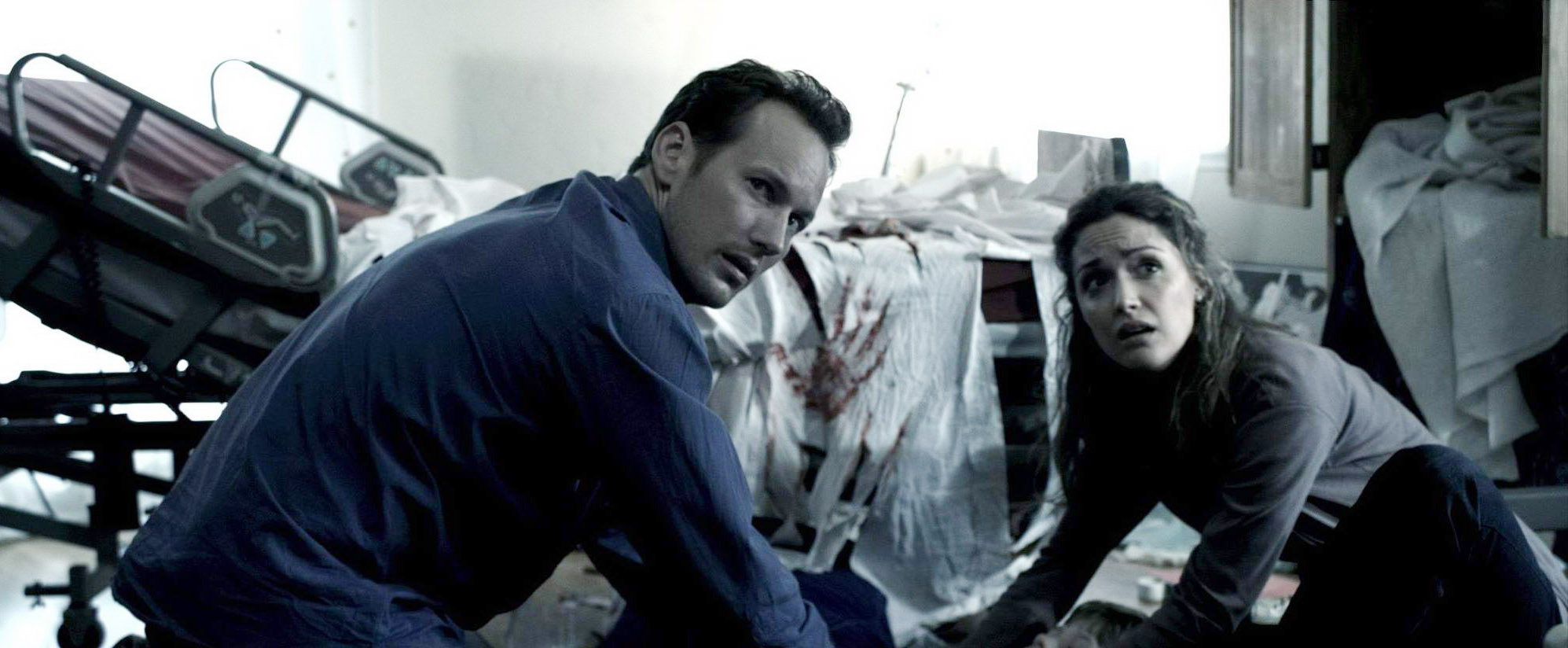 A man kneels alongside a woman and there's a bloody handprint in the back.