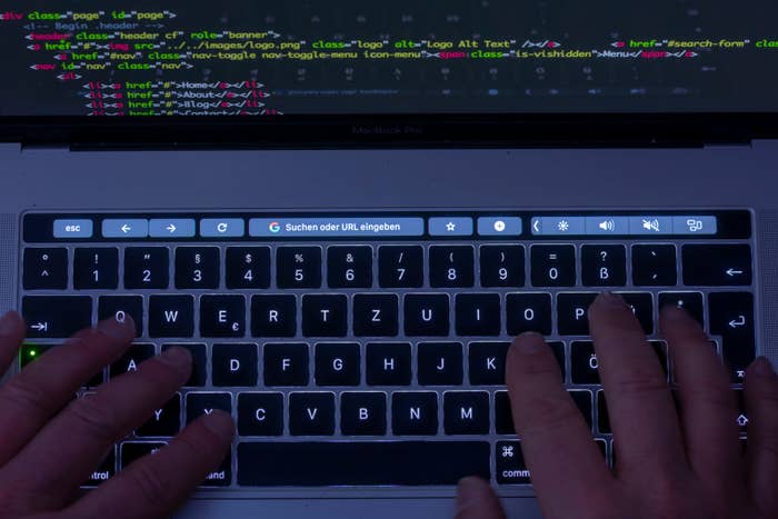 man typing on keyboard with code on screen