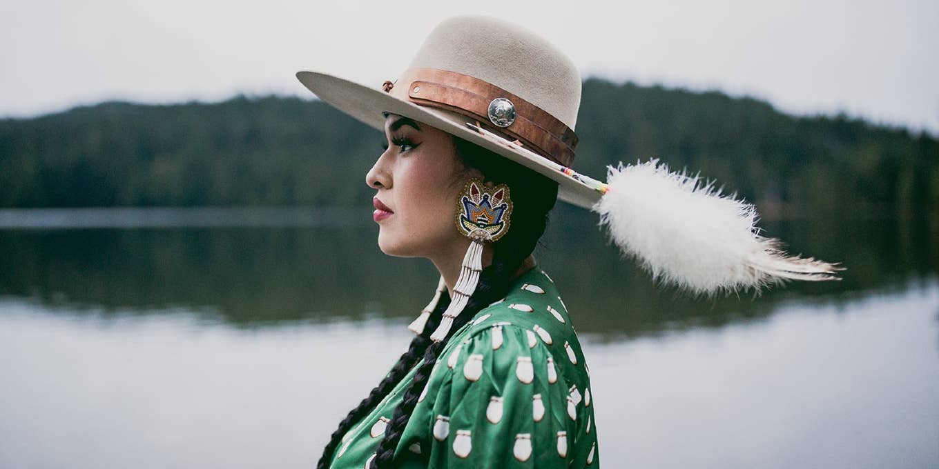 Tia Wood wearing a hat and beadwork earrings, looking to the left