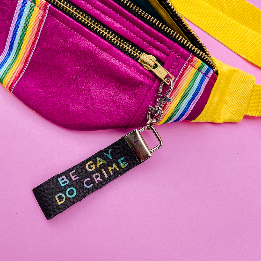 A fuscia and yellow fanny pack with two rainbow stripes, and a keychain reading &quot;be gay do crime&quot;