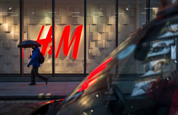 A pedestrian under an umbrella walks past the H&amp;M logo.