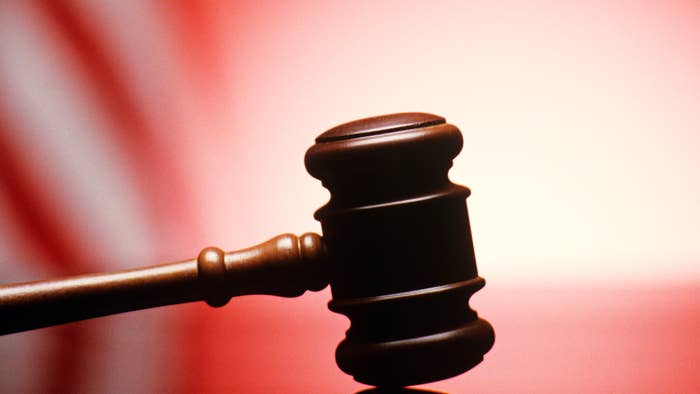 GAVEL RESTING ON REFLECTIVE BENCH SURFACE WITH AMERICAN FLAG IN BACKGROUND.