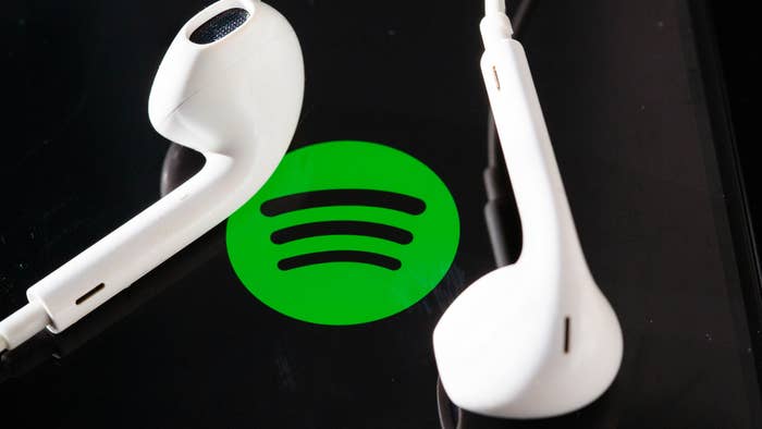 Headphones are on the screen of a smartphone, which displays the Spotify logo