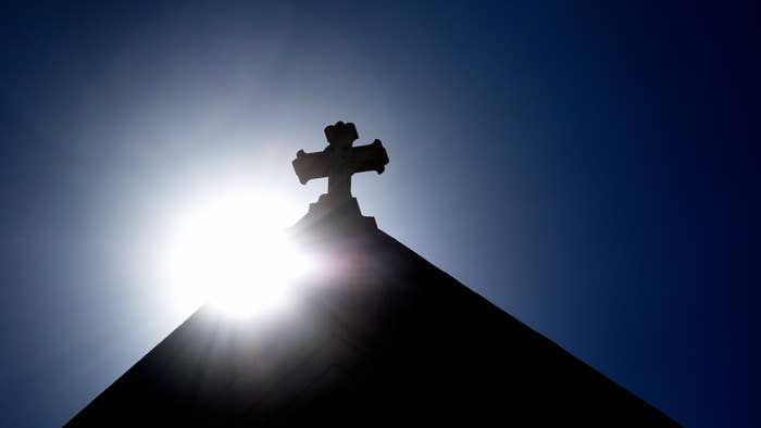 The sun rises behind a stone cross atop the historic Cathedral Basilica of St. Frances of Assisi.