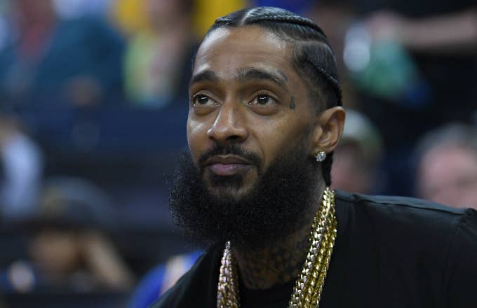 Rapper Nipsey Hussle sitting at courtside looks on during an NBA basketball game