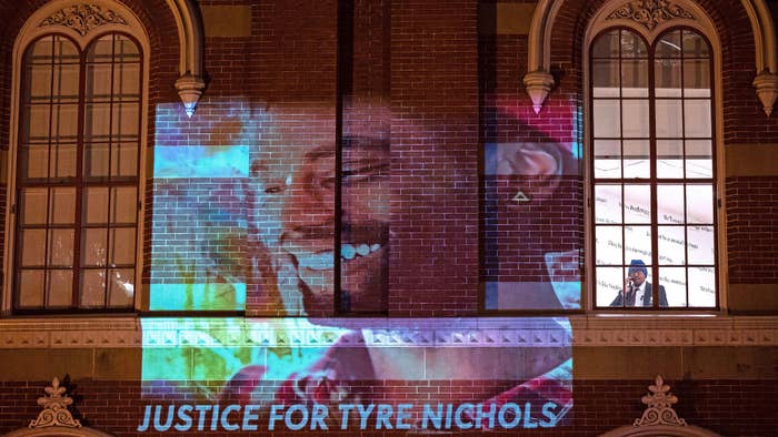 A security guard looks out of a window as protesters project an image of Tyre Nichols