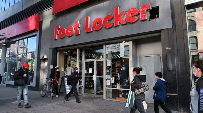 People wearing protective masks walk past a Foot Locker store