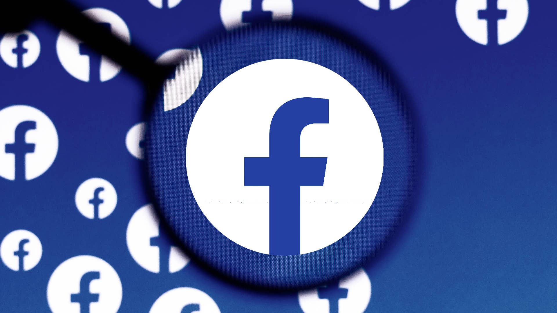 In this photo illustration a Facebook logo is seen on a computer screen through a magnifying glass.