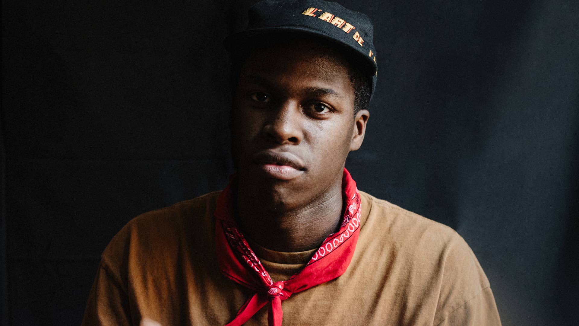 Canadian R&B star Daniel Caesar posing in cap and red bandana