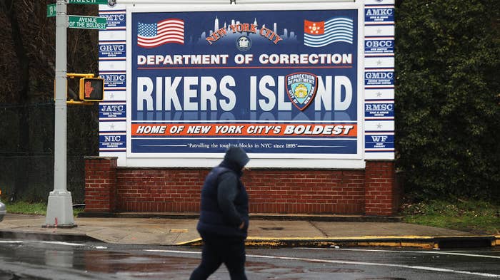A woman walks by a sign at the entrance to Rikers Island