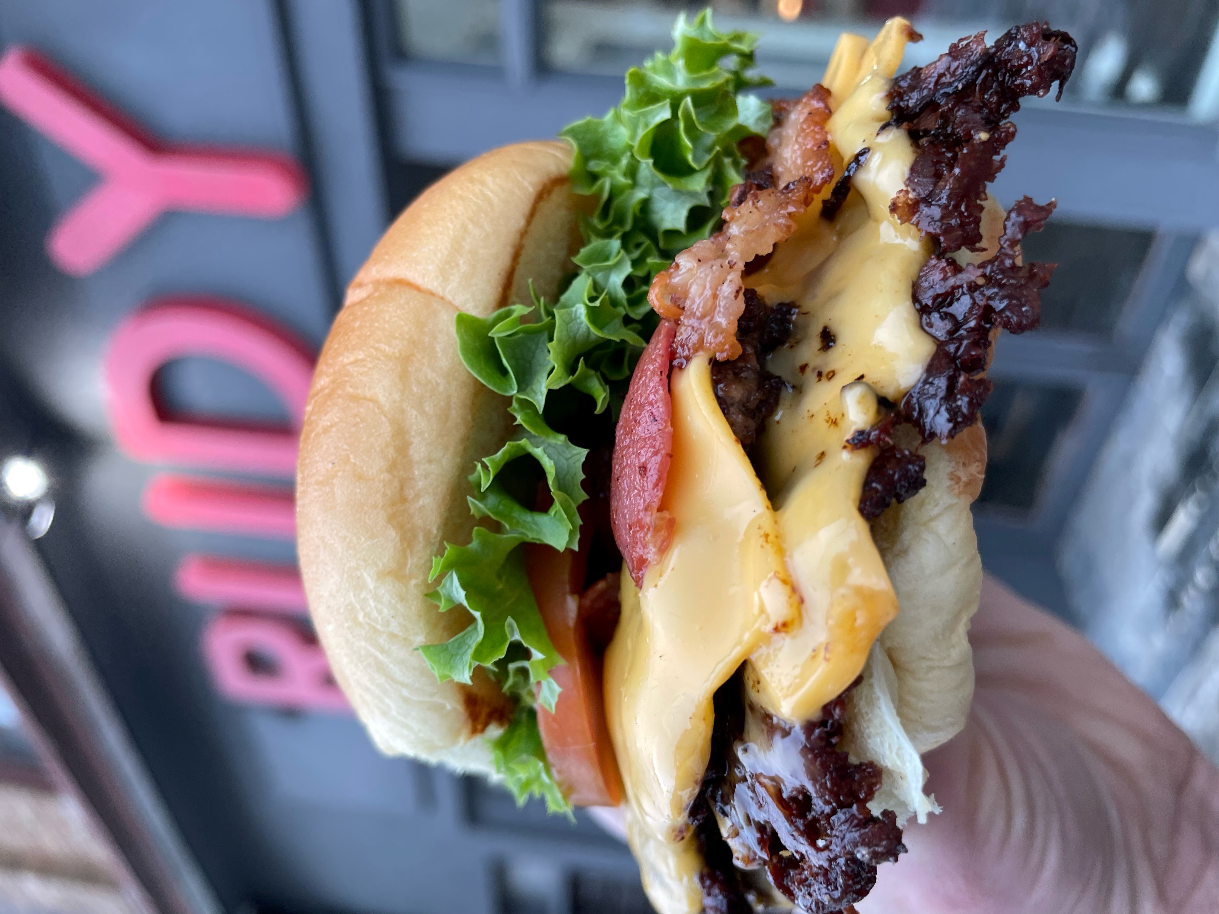 a hand holding a burger outside of rudys