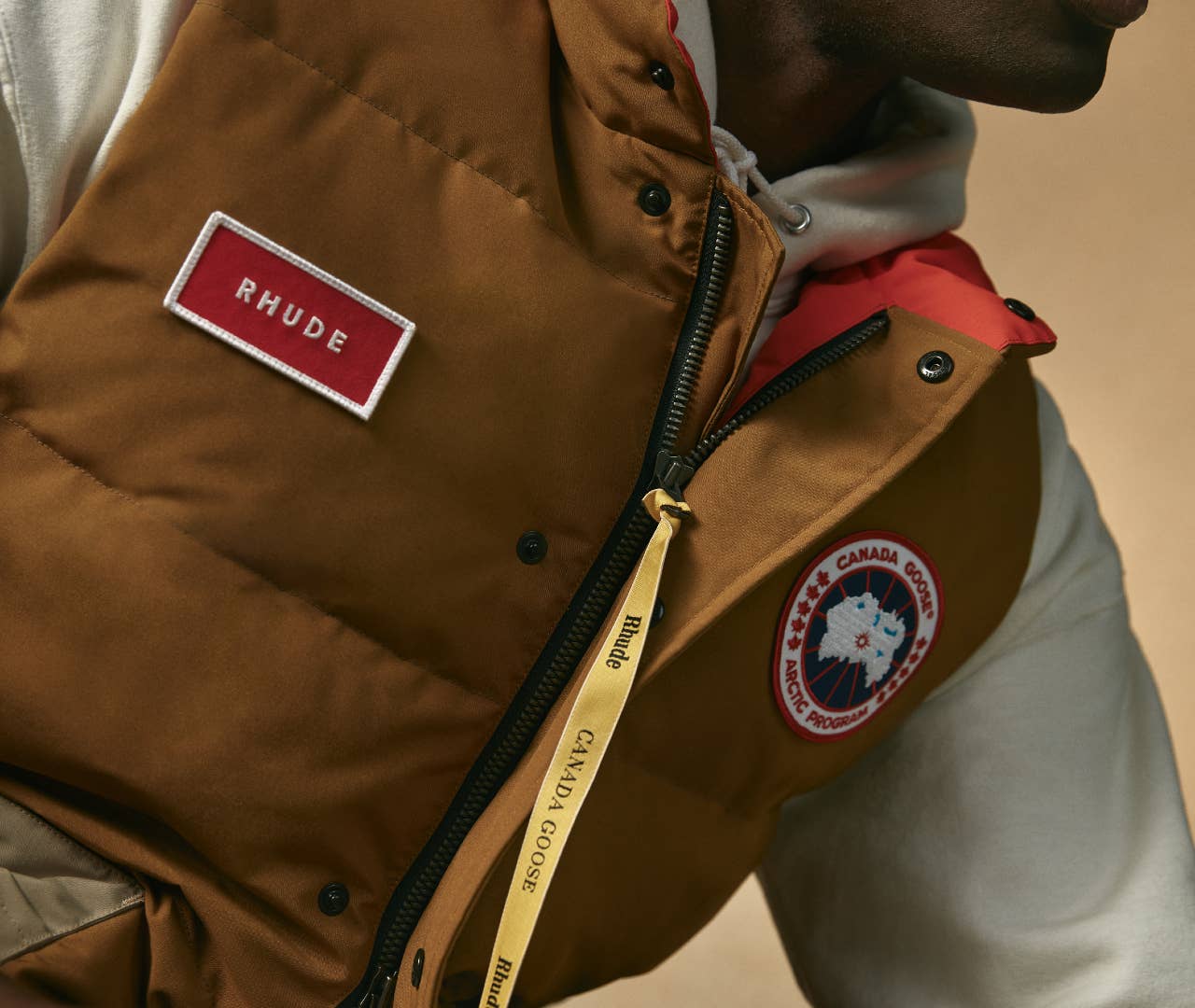 A brown vest worn by a model, with the Canada Goose and RHUDE logos visible