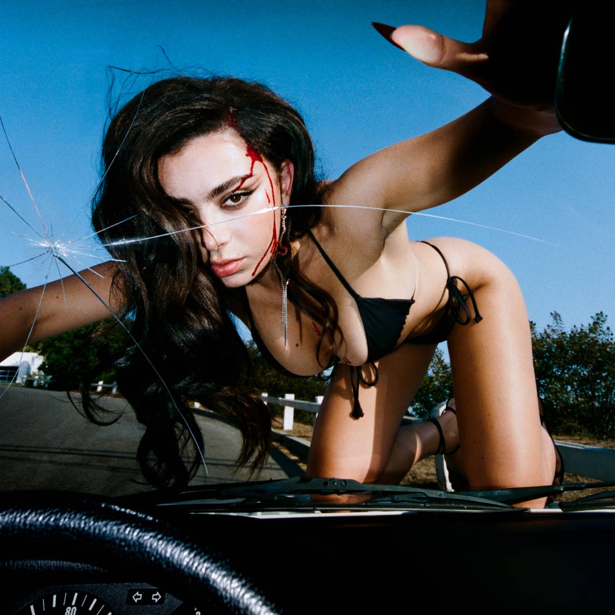 Charli XCX is seen on the hood of a car