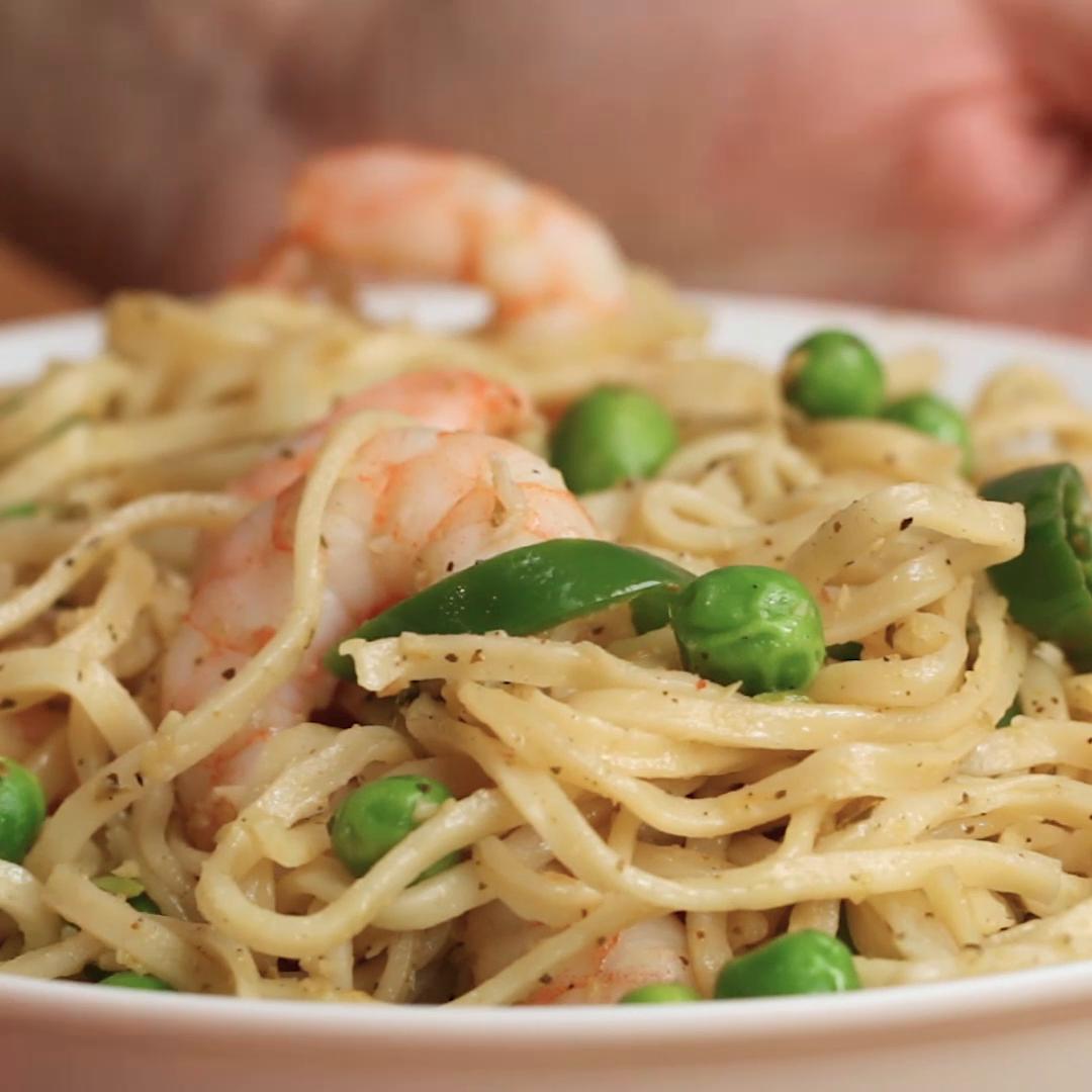 A bowl of noodles with shrimp, peas, and a light seasoning, served in a white dish