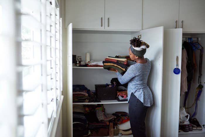 Person organizing a cluttered closet, placing folded clothes on shelves