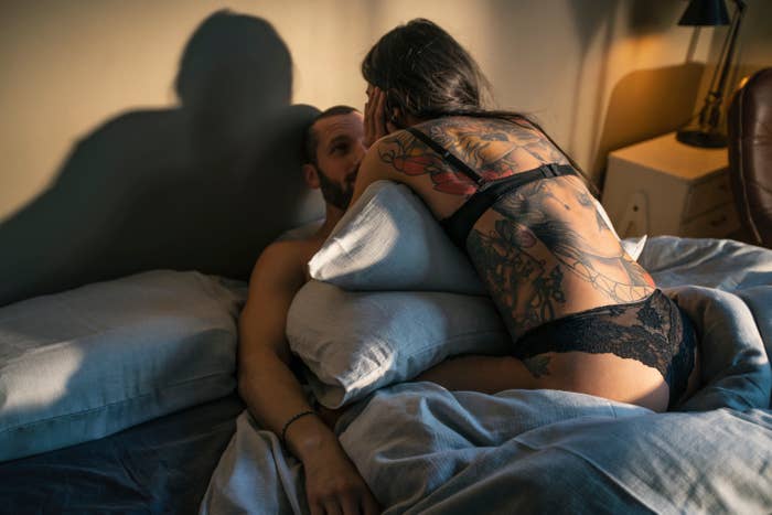 A couple embracing on a bed with the focus on a woman&#x27;s back with a tattoo