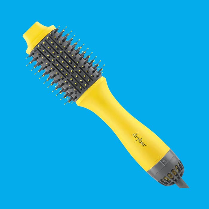 A yellowish  Drybar hairsbreadth  styling brushwood  with a rounded tube  and bristles is shown connected  a plain background