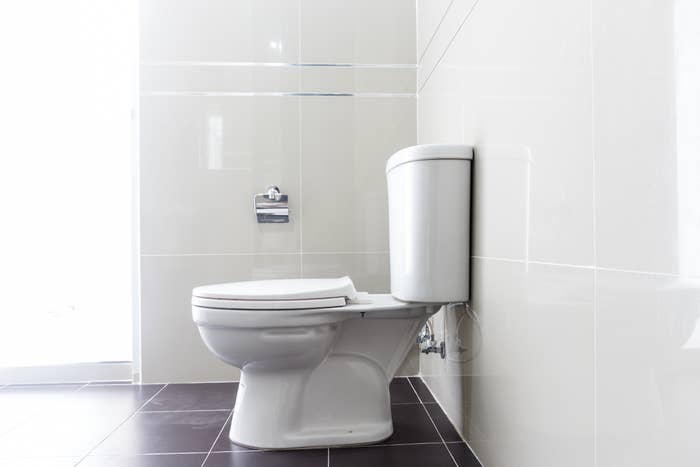A modern, white toilet in a clean, tiled bathroom with a toilet paper holder mounted on the wall beside it