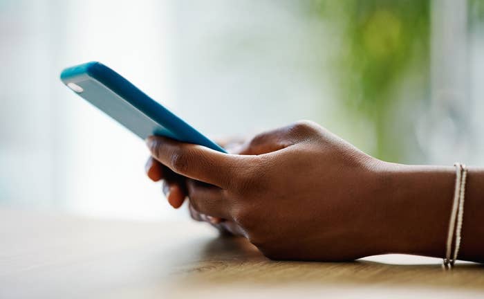 Person holding a smartphone with both hands, looking at the screen. Background is softly blurred, emphasizing focus on the phone