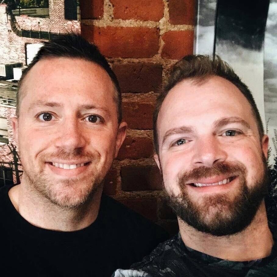 Two smiling people taking a selfie against a brick wall