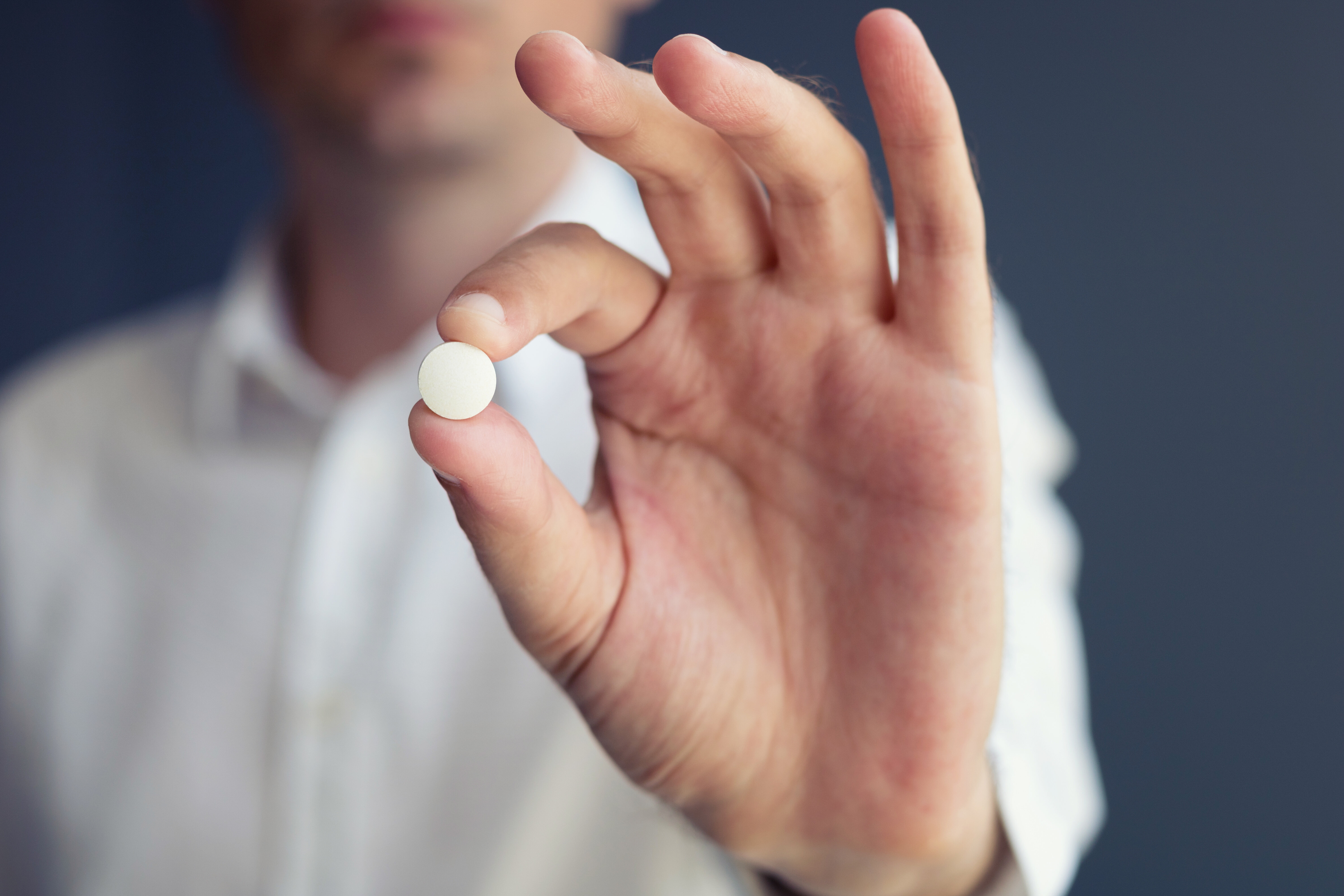 Person holding a pill between thumb and forefinger, focused on pill with blurred background