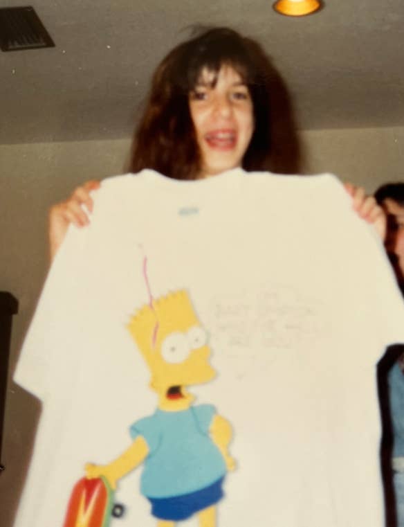 A person holding a large white T-shirt with a Bart Simpson design and a skateboard graphic