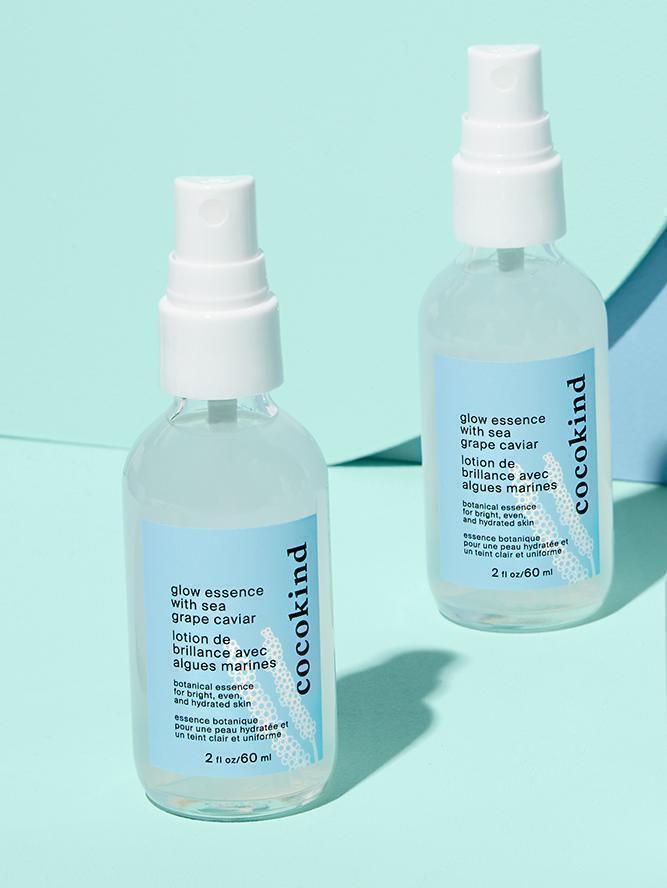 Two bottles of Cocokind glow essence with sea grape caviar are displayed against a simple backdrop