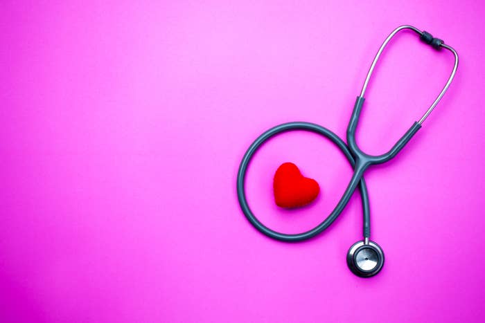 A stethoscope is arranged in a circular shape with a small red heart in the center, set against a plain background. No people are present