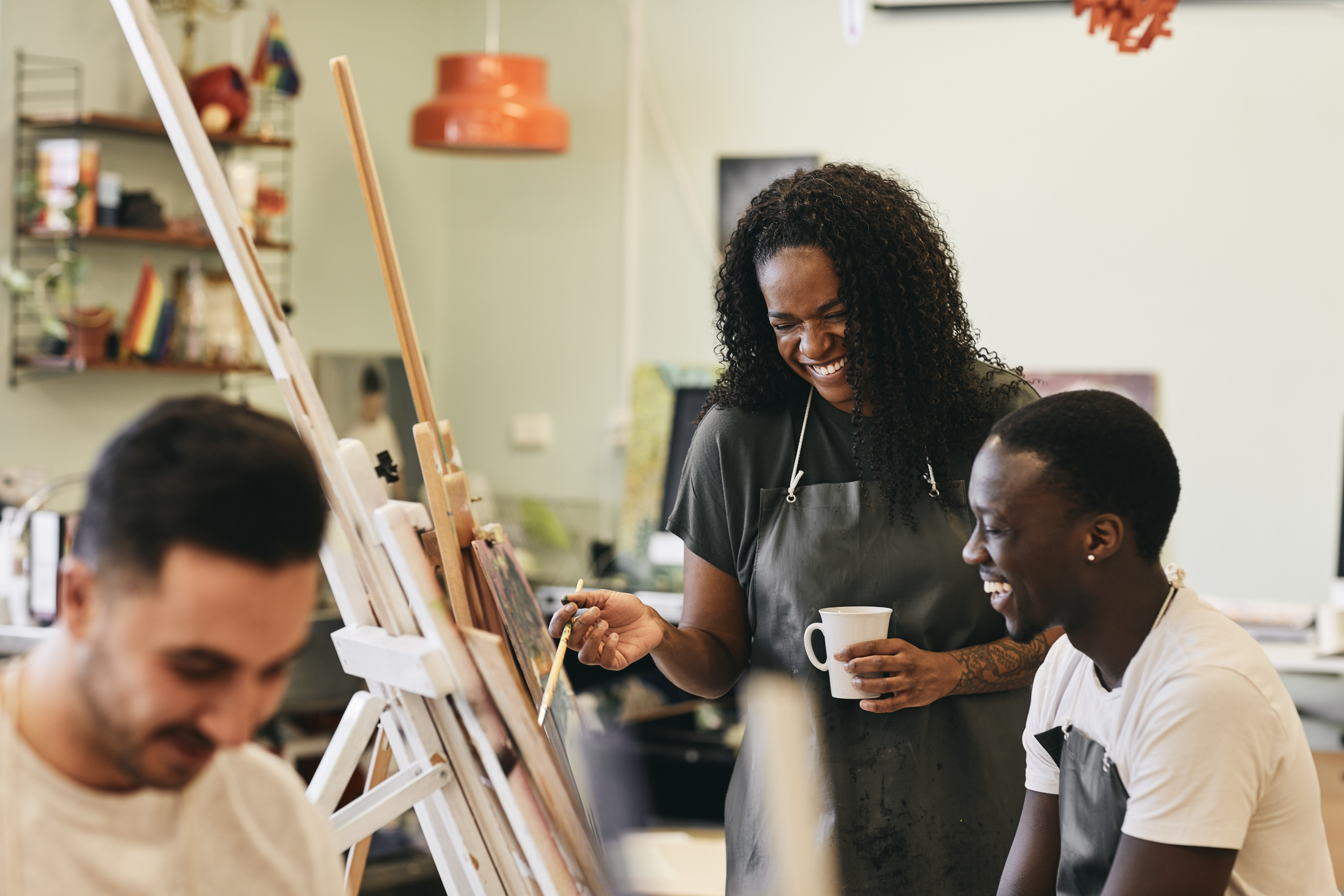 A middle-aged Black woman painting in a class alongside a young man, laughing