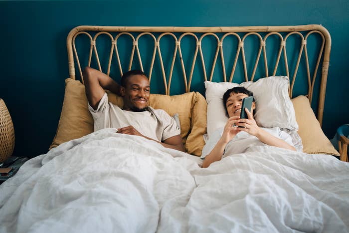 A woman and man laying in bed together as she shows him something on her phone