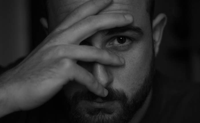 Man peering through fingers covering face, expressing contemplation or secrecy