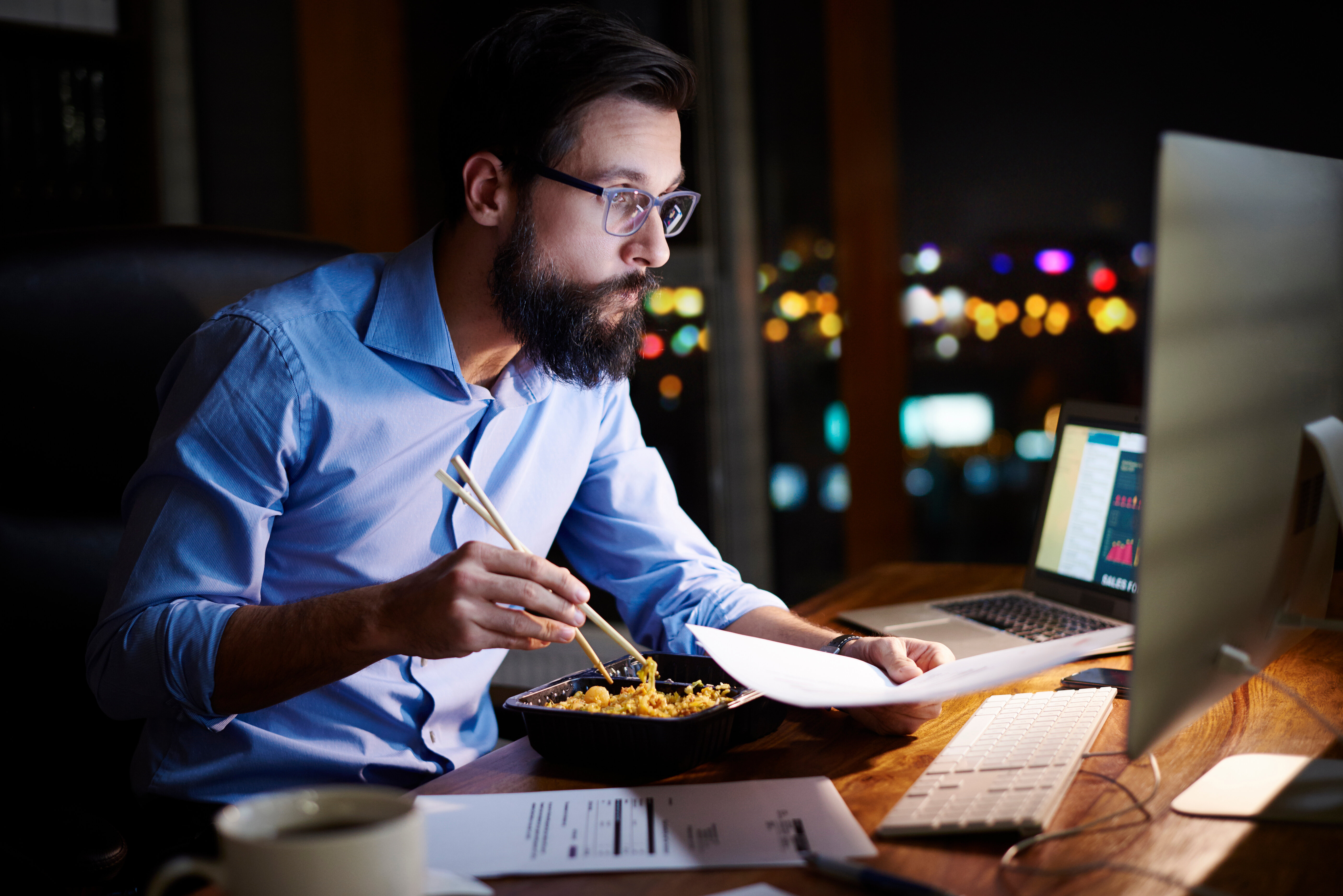 a man eating at his computer desk at night