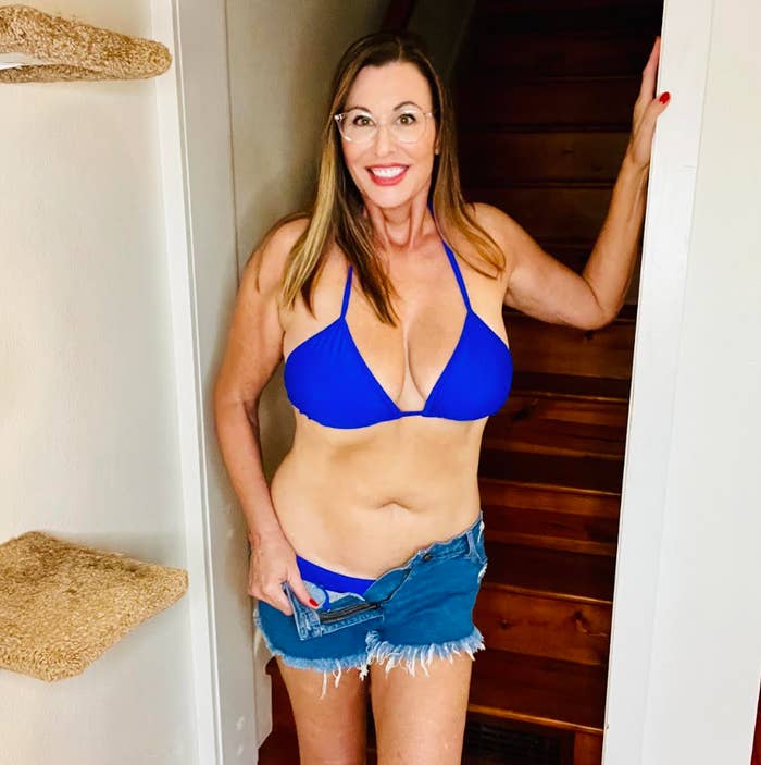 Person smiling in a bikini top and denim skirt, standing in a doorway with relaxed confidence