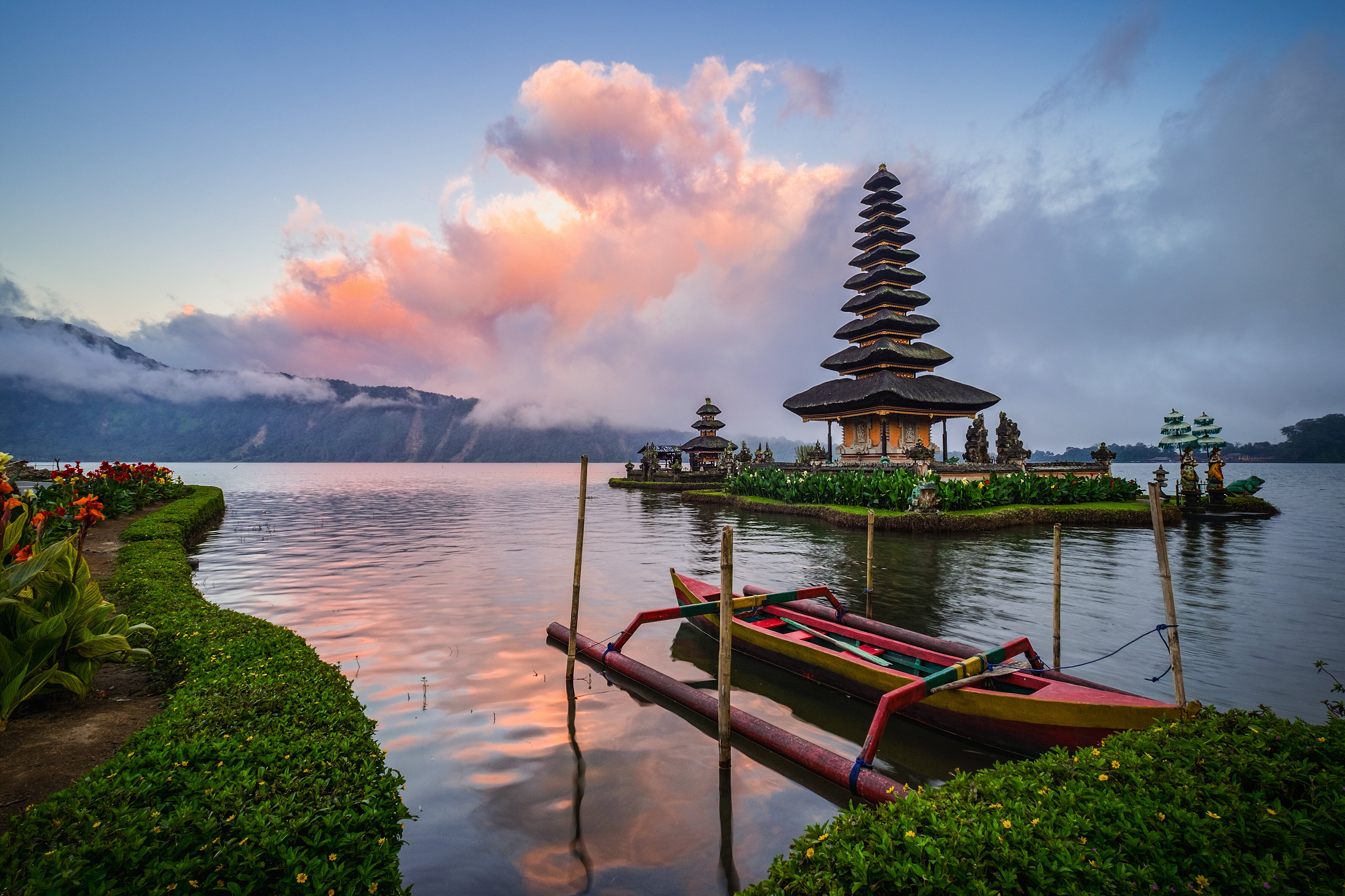 A tranquil lakeside view of Ulun Danu Beratan Temple in Bali with an empty boat and vibrant clouds in the background