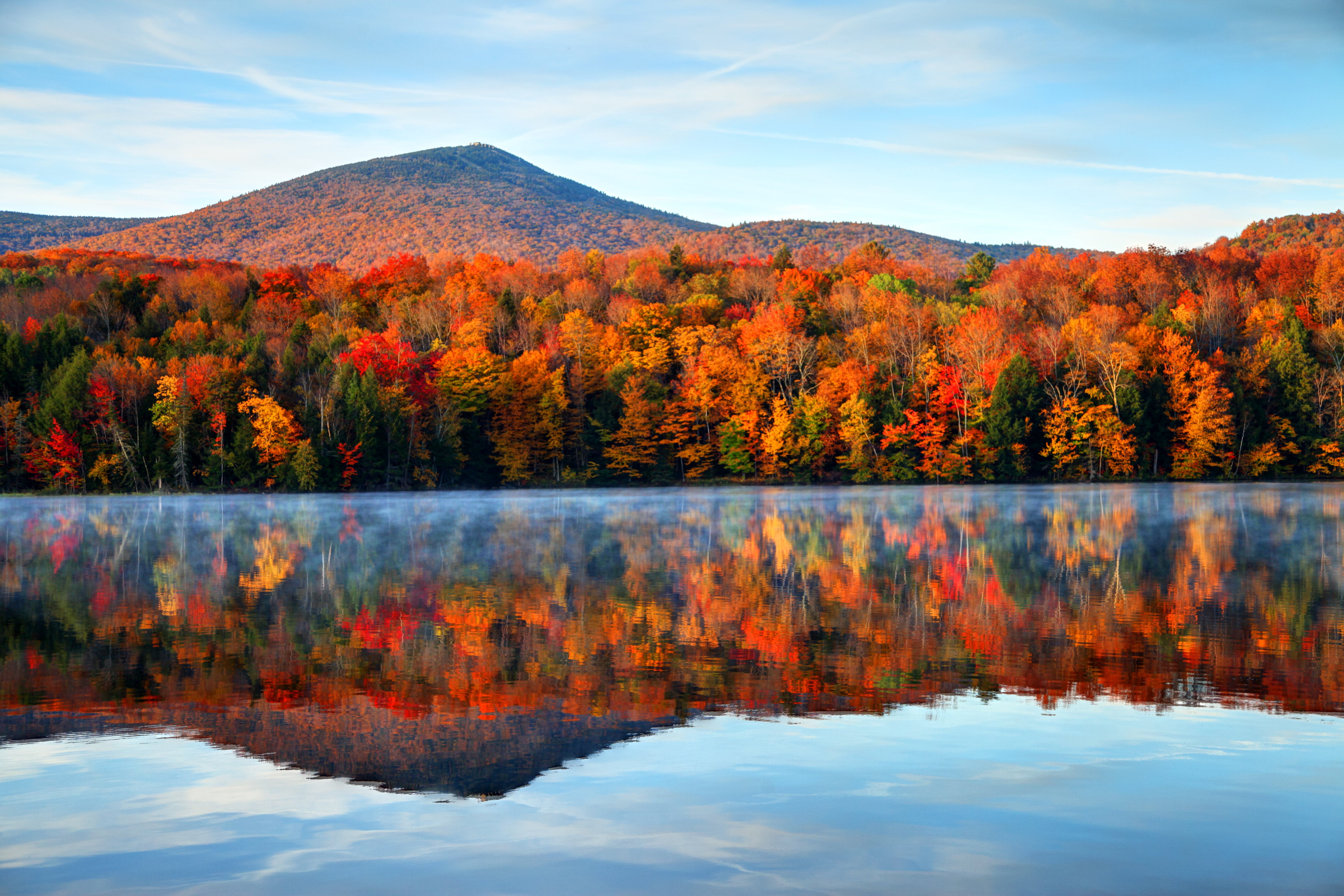 Scenic autumn landscape with vibrant trees reflected in a calm lake, set against a mountainous backdrop