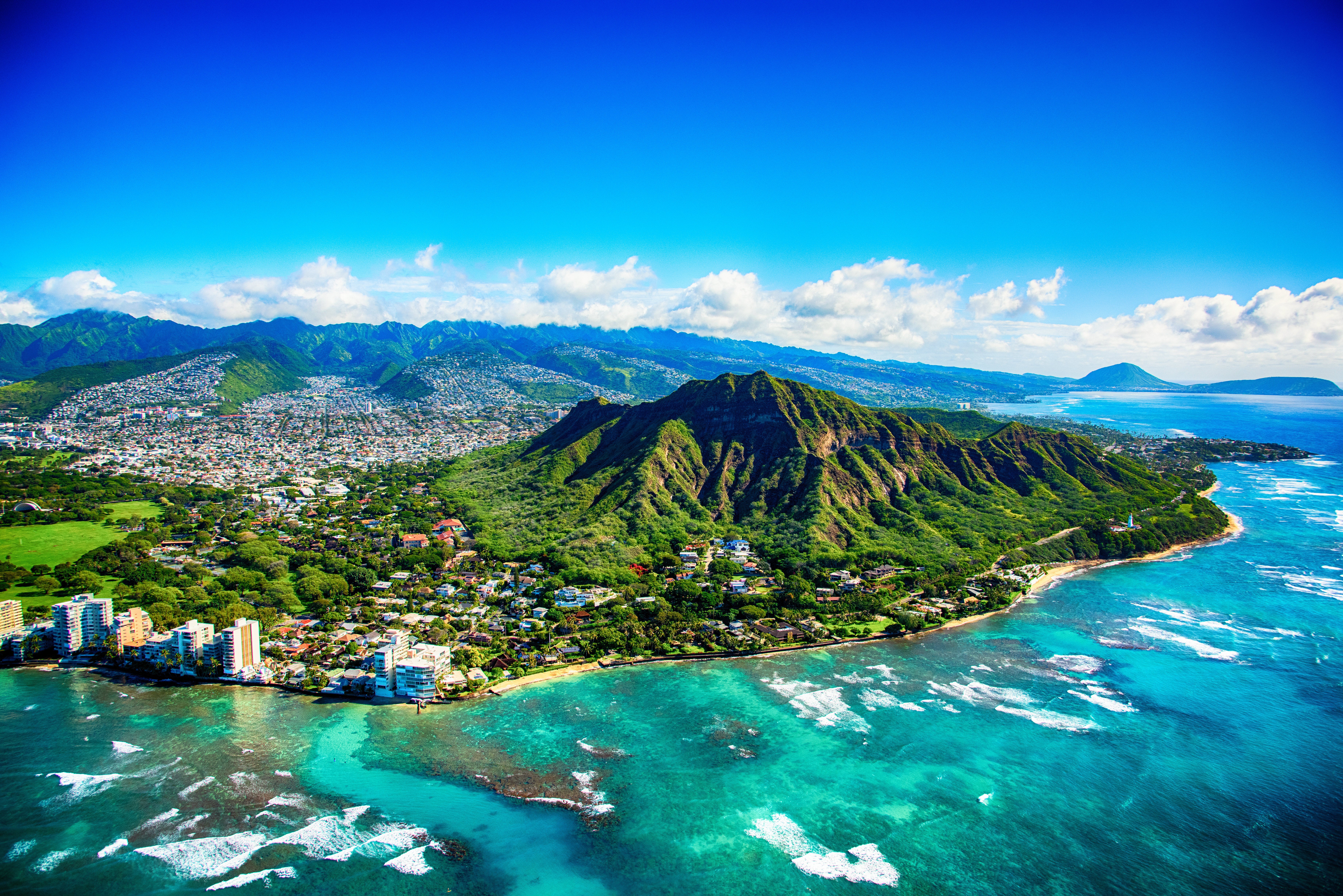 Aerial view of a lush volcanic mountain surrounded by a coastal city with turquoise ocean waves gently lapping against the shoreline