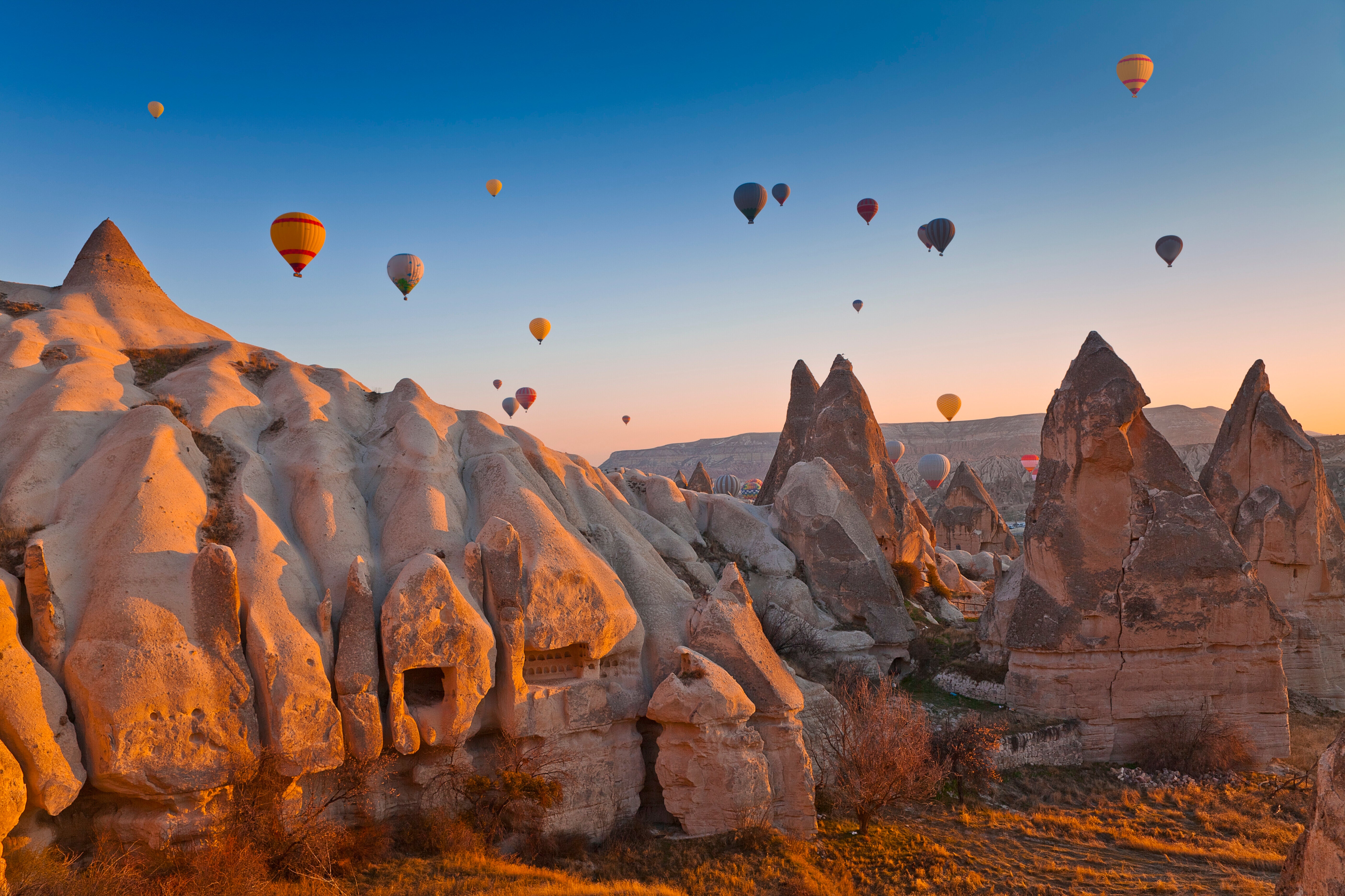 Rocky landscape with unique formations and many hot air balloons floating in the sky during sunrise