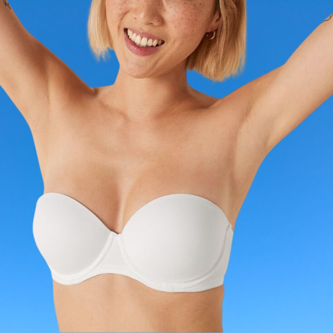 Person wearing a strapless bra, smiling with arms raised against a plain background