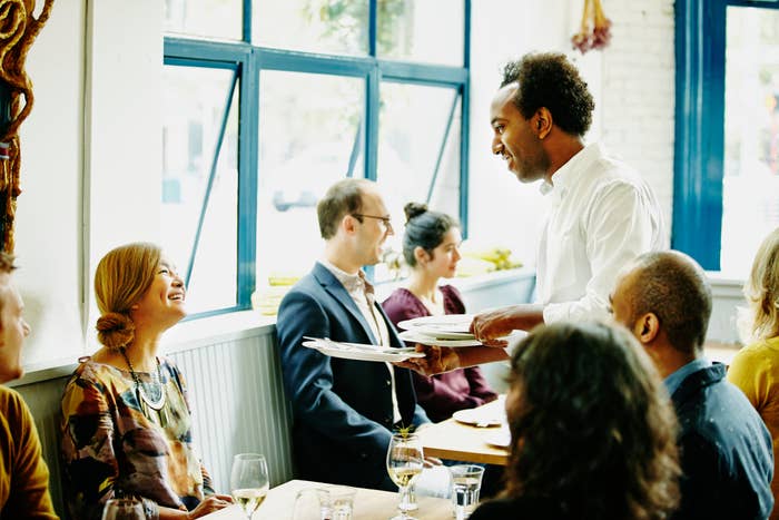 Waiter serving a group of people dining at a restaurant, engaged in conversation and enjoying the experience