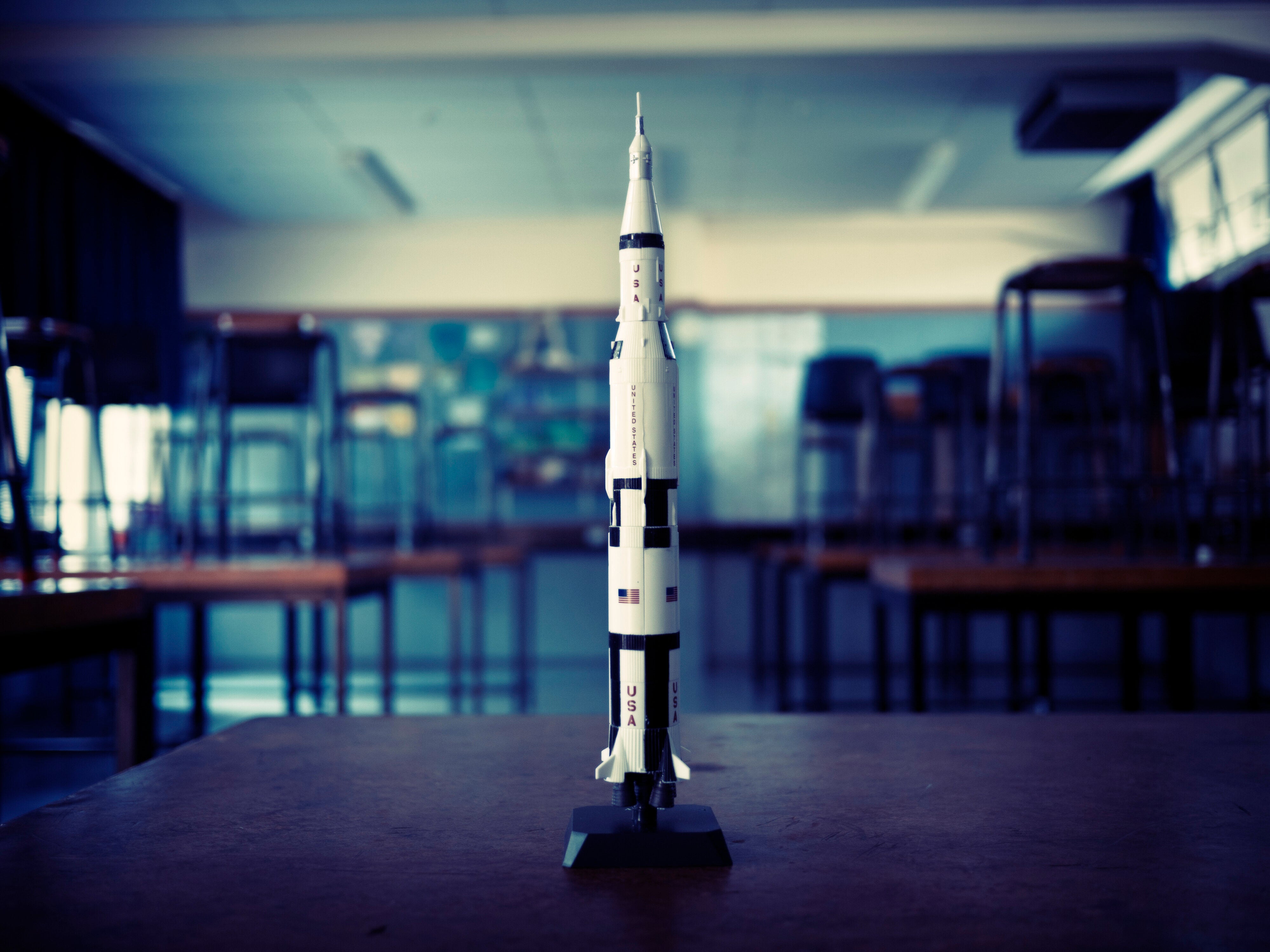 Model rocket of a Saturn V displayed in a classroom setting with desks and chairs in the background
